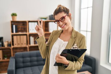 Danışma ofisinde çalışan genç bir kadın kameraya bakıp zafer işareti yapıyor. İki numara.. 