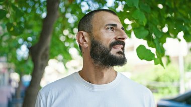 Genç İspanyol bir adam parkta ciddi bir ifadeyle yan tarafa bakıyor.