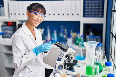 Young beautiful hispanic woman scientist smiling confident using microscope at laboratory