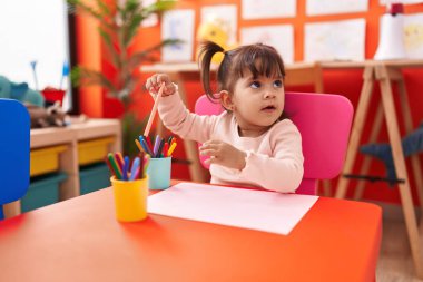 Anaokulunda masaya oturmuş kağıda resim çizen sevimli İspanyol kız öğrenci.