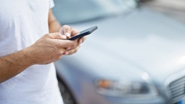 Genç İspanyol adam akıllı telefon kullanıyor. Arabasının yanında bekliyor.