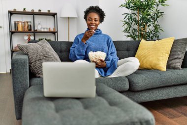Afro-Amerikalı kadın evde kanepede oturmuş film izliyor.