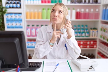Eczanede çalışan genç, beyaz bir kadın telefonla konuşuyor. Kuşkular üzerine yoğunlaşmış, çenesi açık ve kafasını kaldırıp, 