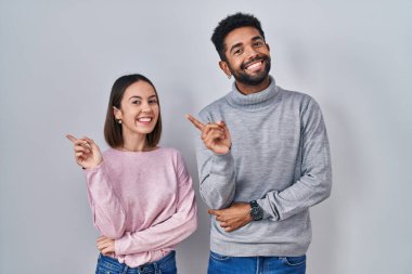 Genç İspanyol çift, yüzünde kocaman bir gülümsemeyle ayakta duruyor. Elleriyle kameraya doğru işaret ediyorlar.. 