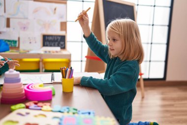 Anaokulunda rahat bir ifadeyle masada oturan sevimli beyaz çocuk.