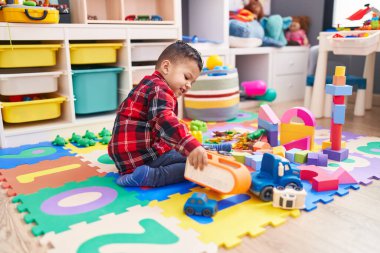 Anaokulunda yerde oturan sevimli İspanyol çocuk araba oyuncağıyla oynuyor.