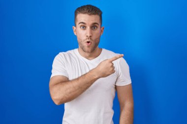 Mavi arka planda dikilen genç beyaz adam parmağını yana çevirerek şaşırdı, ağzı açık hayret içinde kaldı.. 