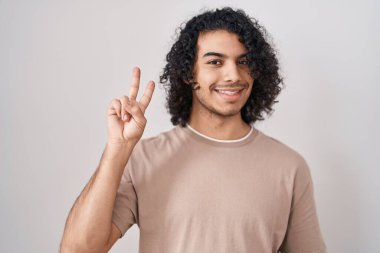 Beyaz arka planda kıvırcık saçlı İspanyol adam kameraya bakıp zafer işareti yapıyor. İki numara.. 