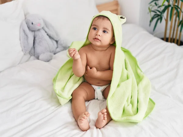 ベッドルームでベッドに座っているカエルタオルを身に着けている愛らしいヒスパニック系の赤ちゃん — ストック写真