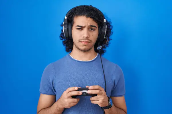 Hispanic Man Curly Hair Playing Video Game Holding Controller Skeptic — Zdjęcie stockowe