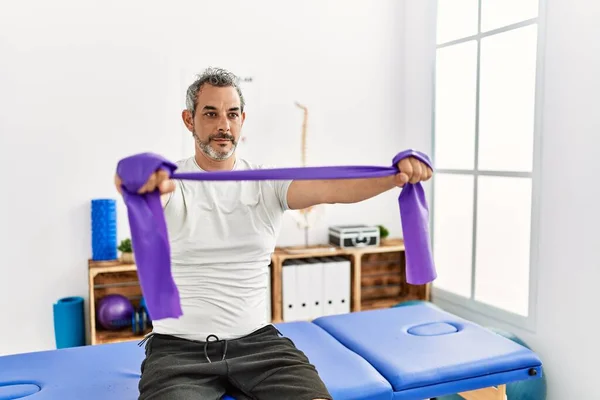 Middle age grey-haired man patient having rehab using elastic band at rehab clinic