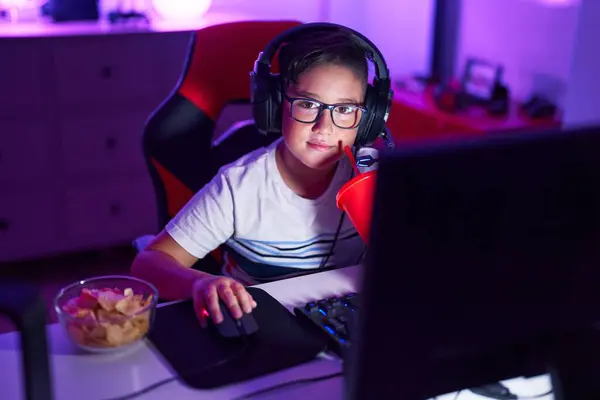 Adorable hispanic boy streamer playing video game drinking beverage at gaming room
