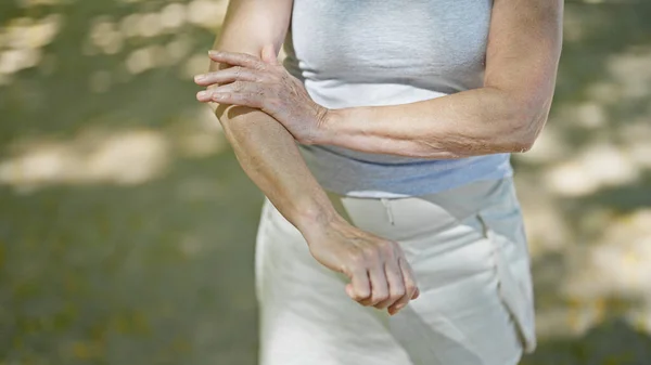 Middle age woman scratching arm at park