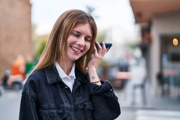 Young blonde woman listening to voice message at street