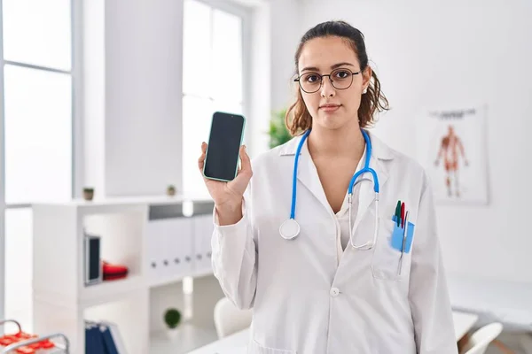 Young Hispanic Doctor Woman Holding Smartphone Showing Screen Thinking Attitude — Stock Photo, Image