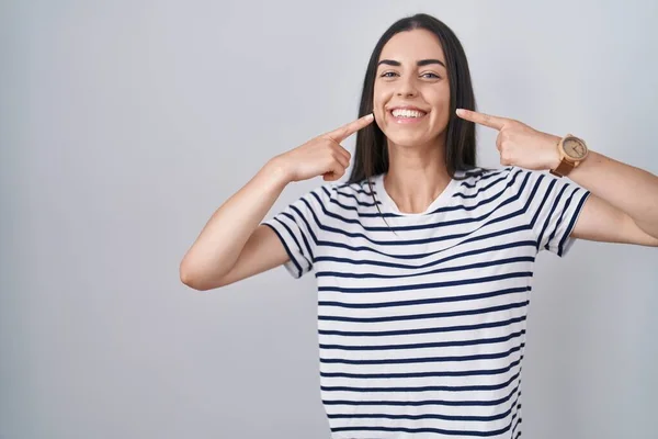 若いブルネットの女性は ストライプのTシャツを着て陽気な表情をし 指の歯と口を指しています 歯科健康コンセプト — ストック写真