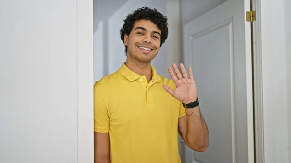 Jovem Latino Sorrindo Confiante Dizendo Olá Com Mão Casa — Fotografia de Stock