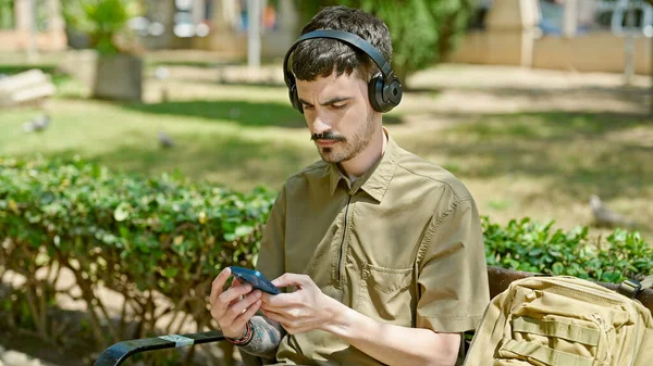 Joven Hispano Usando Smartphone Auriculares Sentados Banco Del Parque — Foto de Stock