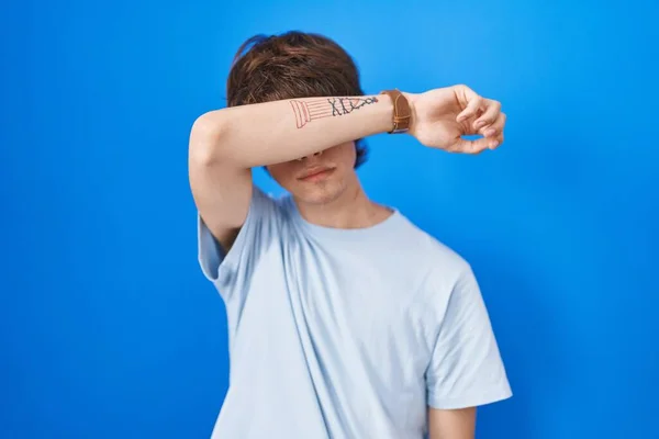 Hispanic Young Man Standing Blue Background Covering Eyes Arm Looking — Φωτογραφία Αρχείου