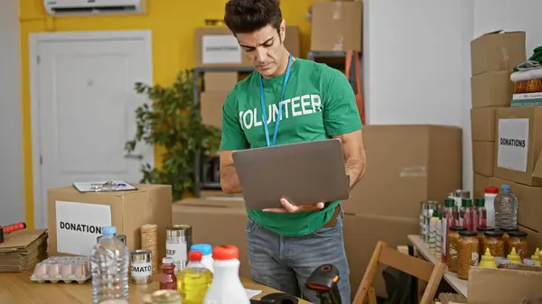 Young Hispanic Man Volunteer Using Laptop Checking Products Charity Center — Stock Photo, Image