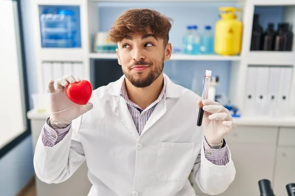 科学者の研究室で働いているひげを持つアラブ人男性は 側面を見つめて見つめる笑顔の血液サンプルを保持し 遠くに考えている — ストック写真