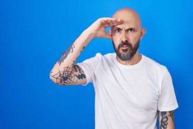 Mavi arka planda dikilen İspanyol dövmeli adam. Alnındaki sorun yüzünden endişeli ve stresli. Kriz için endişeli. 