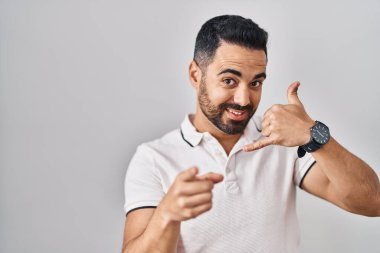 Beyaz arka planda günlük giysiler giyen, gülümseyen, telefonda konuşan ve seni işaret eden Latin kökenli genç bir adam. Ara beni.. 