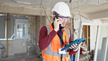 Genç İspanyol müteahhit inşaat alanındaki touchpad kullanarak akıllı telefondan konuşuyor.