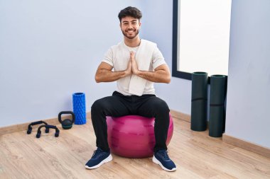 Sakallı İspanyol bir adam yoga odasında pilatese oturmuş elleriyle dua ediyor ve kendinden emin bir şekilde af diliyor.. 