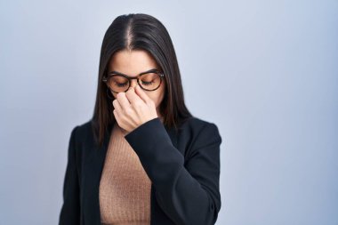 Mavi arka planda duran esmer kadın yorgun burnu ve gözleri ovuşturup yorgun ve baş ağrısı çekiyor. Stres ve hüsran kavramı. 