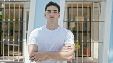 Ciddi bir ifadeyle ve kollarını kavuşturarak sokakta dikilen İspanyol genç bir adam.