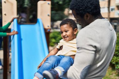 Baba ve oğul oyun alanında kaydırak oynuyorlar.