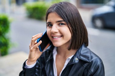 Genç, güzel, İspanyol bir kadın gülümsüyor ve caddede akıllı telefondan konuşuyor.