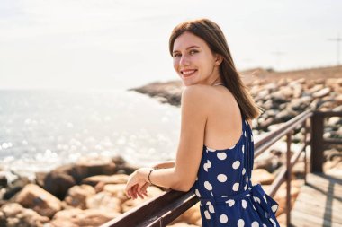 Genç sarışın kadın turist gülümsüyor. Kendine güvenen, deniz kenarındaki balyalara yaslanan.