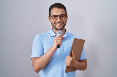 İspanyol adam elinde mikrofon ve pano tutarken yüzünde mutlu ve havalı bir gülümsemeyle gülümsüyor. diş gösterme. 