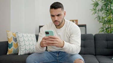 Genç İspanyol adam evde akıllı telefon kullanarak kanepede otururken strese girdi.