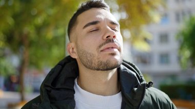 Young hispanic man breathing with closed eyes at park