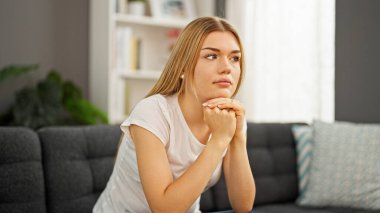Young blonde woman sitting on sofa with serious expression at home