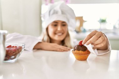 Aşçı üniforması giyen genç bir kadın mutfakta kekin üzerine ahududu koyuyor.