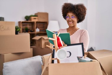 Afro-Amerikalı bir kadın gülümseyerek evde kendinden emin bir şekilde kitap okuyor.