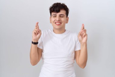 Gündelik beyaz tişört giyen, umut ve gözlerin kapalı gülümseyerek el hareketi yapan genç bir adam. Şans ve batıl inançlar. 