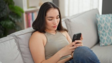 Evdeki kanepede oturan akıllı telefon kullanan genç, güzel İspanyol kadın.