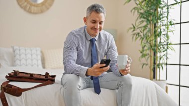 Genç İspanyol iş adamı akıllı telefon kullanıyor otel odasında kahve içiyor.