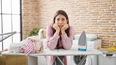 Genç ve güzel İspanyol kadın çamaşırhanede üzgün bir ifadeyle ütü masasına yaslanıyor.