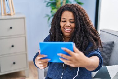 African american woman watching video on touchpad sitting on sofa at home