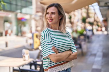 Kendine güvenen genç bir kadın caddede kollarını kavuşturmuş duruyor.