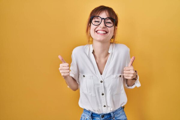 Young beautiful woman wearing casual shirt over yellow background success sign doing positive gesture with hand, thumbs up smiling and happy. cheerful expression and winner gesture. 