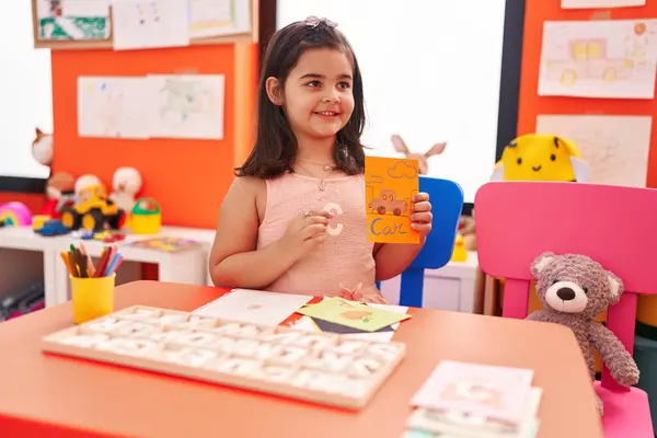 Adorable hispanic girl playing with vocabulary puzzle game sitting on table at kindergarten