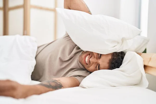 African american man suffering for noise covering ears with pillow at bedroom