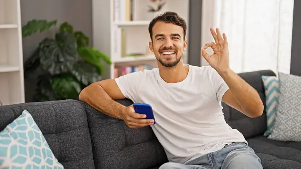Young Hispanic Man Using Smartphone Doing Gesture Home — Stockfoto